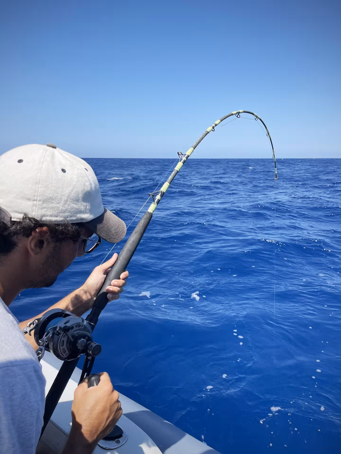 Angler battles a fish on a private Sant'Antioco fishing charter, surrounded by deep blue ocean waters.