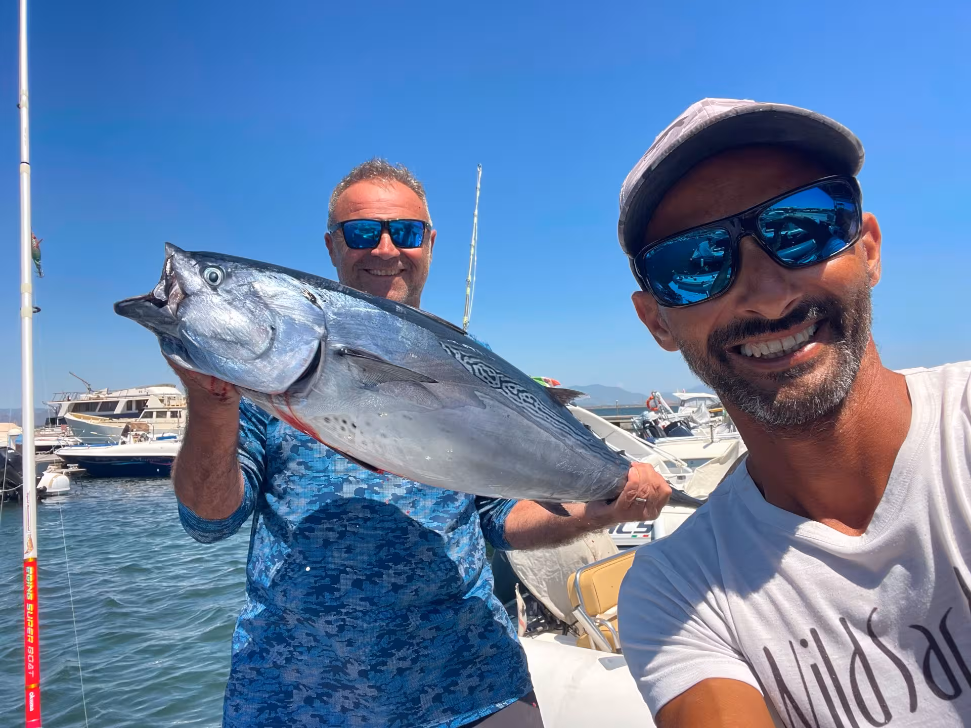 Smiling anglers showcase a large catch on a Sant'Antioco private fishing charter under a sunny blue sky.