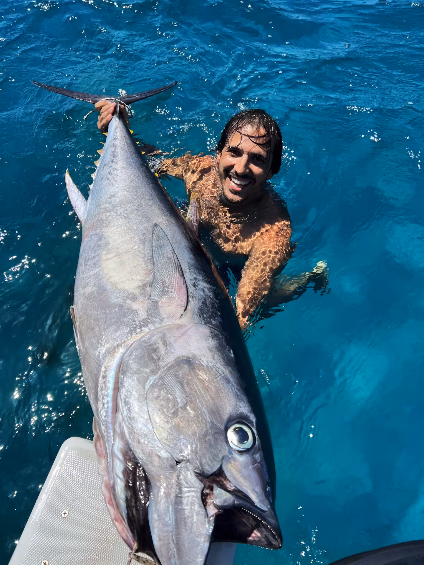 Excited angler holds a massive tuna on a private fishing charter in Sant'Antioco's clear blue waters.