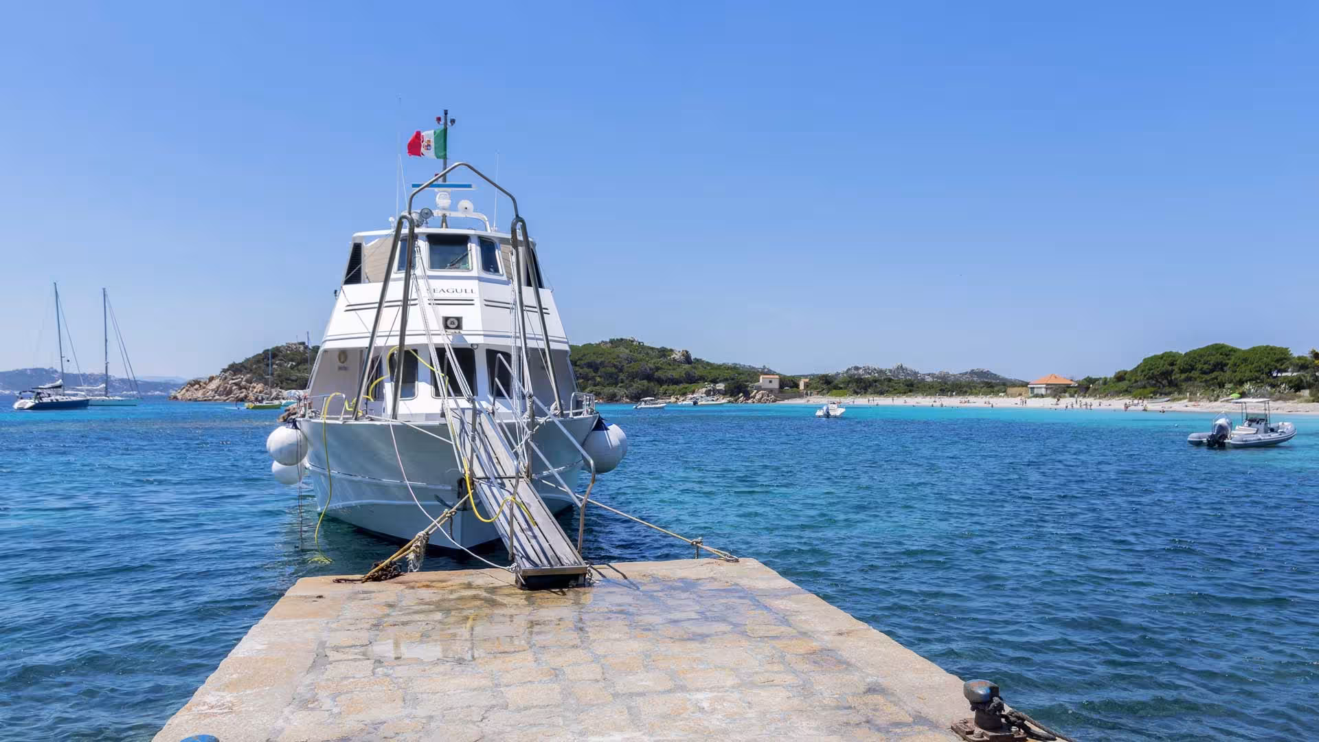 Docked motorboat at Santa Teresa di Gallura pier ready for La Maddalena Archipelago tour under a clear blue sky.