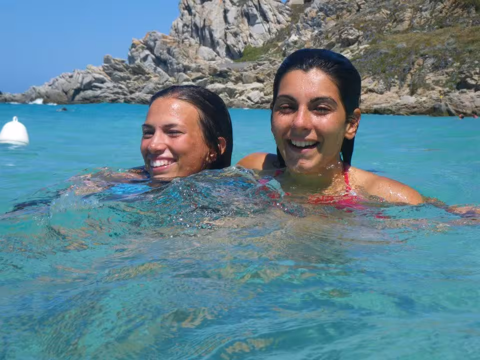 Two friends swimming in the turquoise waters of Santa Teresa di Gallura, surrounded by rocky coastal landscapes.
