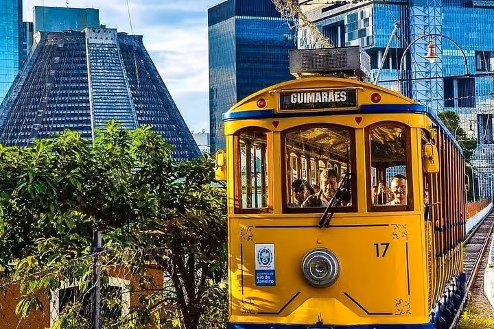Historic yellow tram in Rio de Janeiro's Santa Teresa neighborhood with modern cityscape in the background.