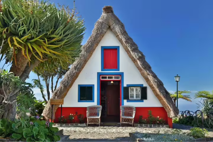 Traditional Santana house with thatched roof in Madeira, surrounded by lush greenery, perfect for a self-drive tour.