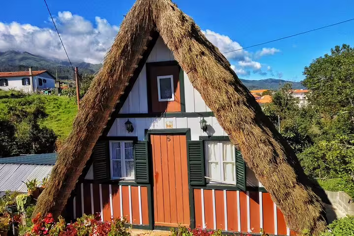 Traditional Santana house in Northeast Madeira with thatched roof, surrounded by lush greenery, perfect for guided tour exploration.
