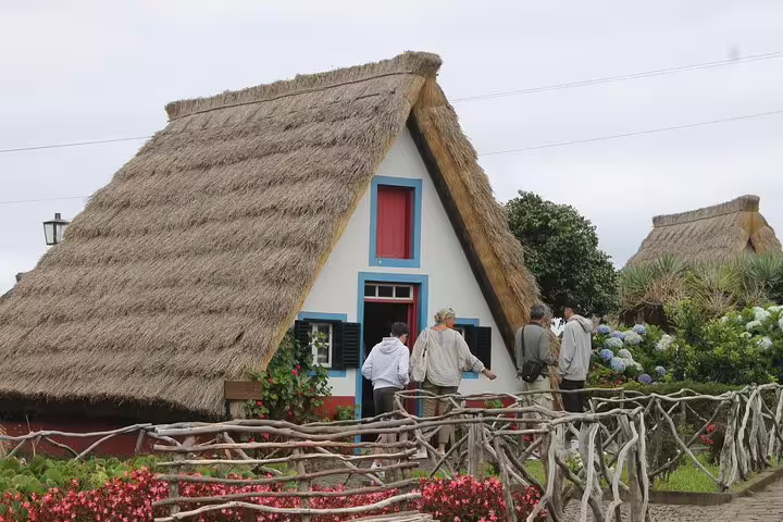 Tourists explore traditional thatched Santana houses on the scenic Northeast 4x4 tour, showcasing Madeira's unique cultural heritage.
