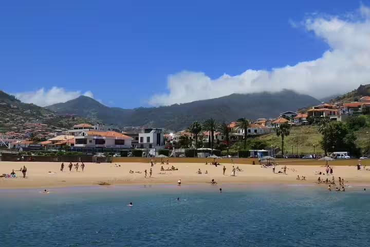 Sandy beach with people enjoying water activities, backed by lush hills and charming houses on the Santana & Peaks 4x4 tour.