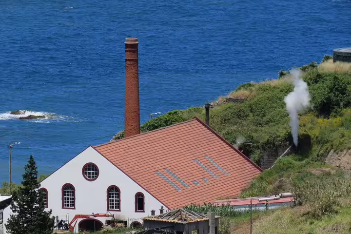 Scenic view of a historic coastal building with a chimney in Santana, surrounded by lush greenery and ocean, on a 4x4 tour.