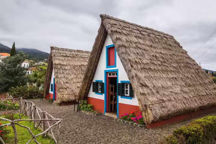 Traditional Santana houses with thatched roofs on a cloudy day, featured in the full-day Pico do Arieiro tour.