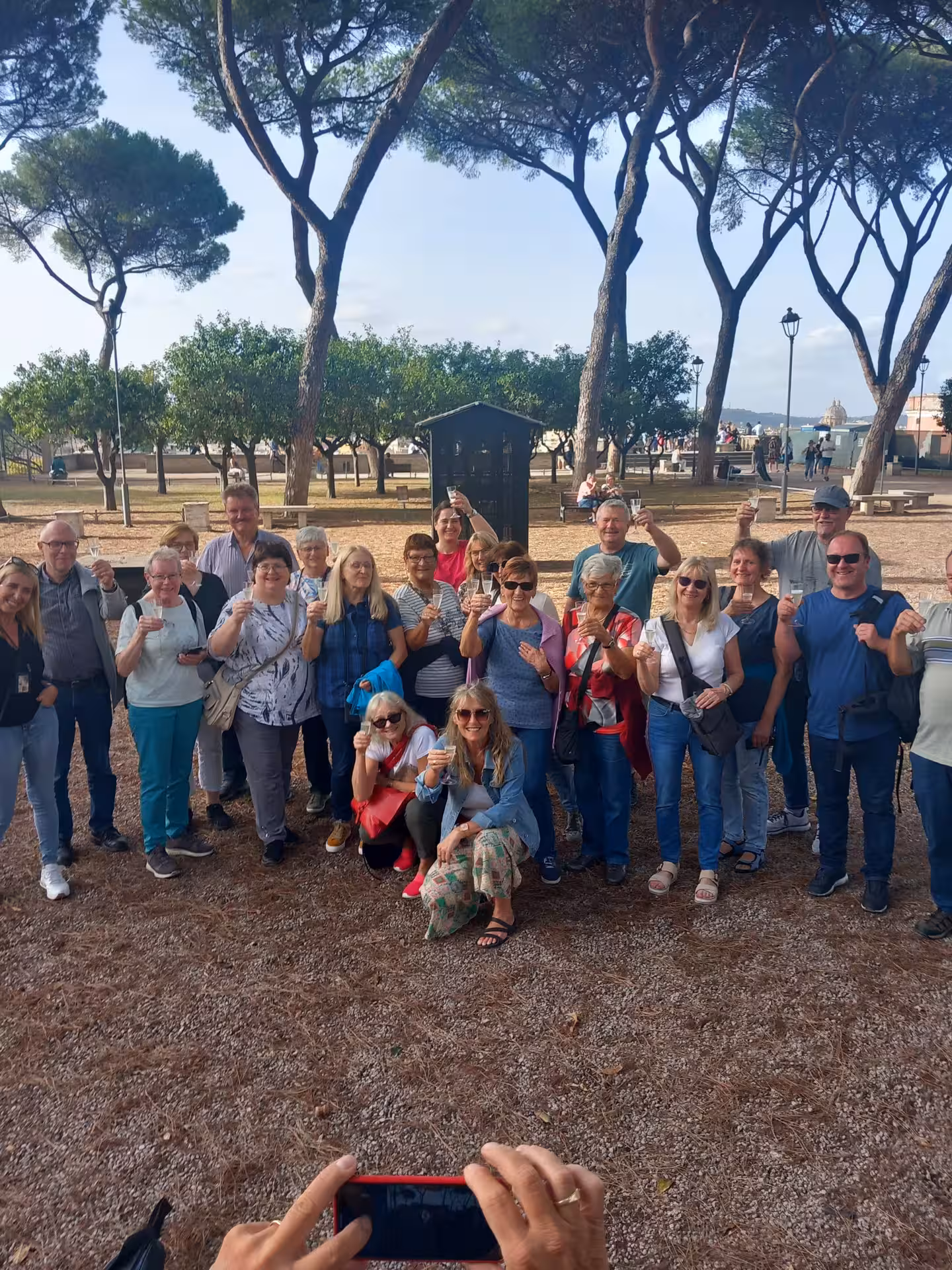 A group of tourists gathers under scenic trees, capturing memories on the Sant'Angelo Castle Combo Tour in Rome.