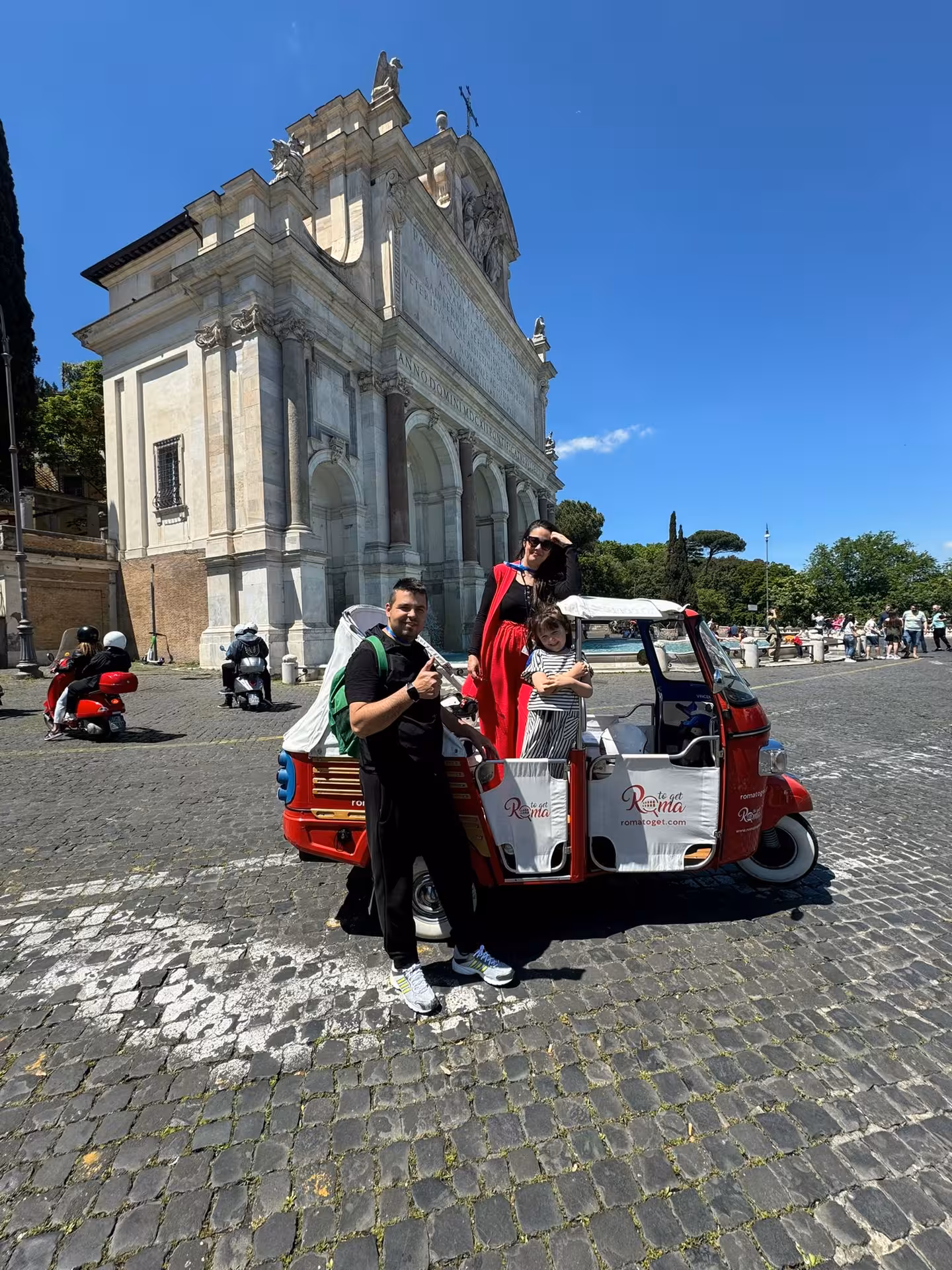 Visitors posing with a red tuk-tuk near a historic Roman church on the Sant'Angelo Castle Combo Tour.