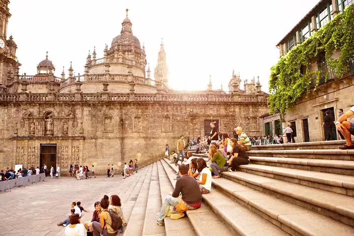 Tourists relax on steps outside the historic cathedral in Santiago de Compostela, a key stop on the Porto to Santiago tour.