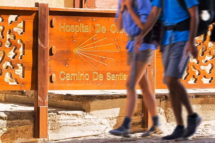 Pilgrims walk past the Hospital de Órbigo sign on the Camino de Santiago during a guided city tour in Santiago de Compostela.