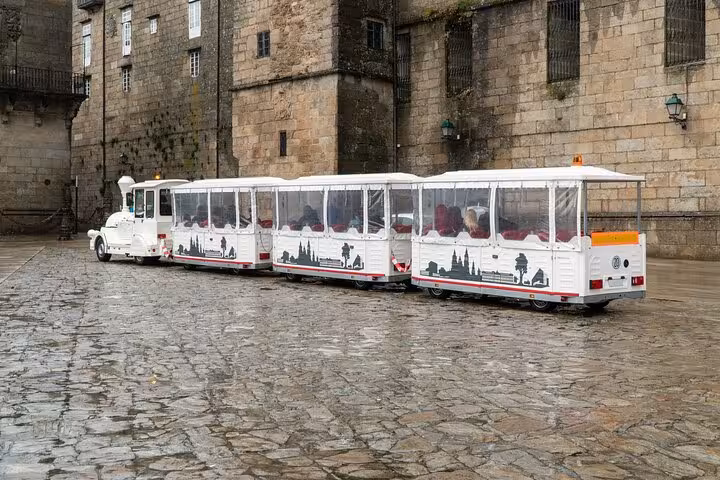 White tourist train parked on cobblestone street in Santiago de Compostela, ideal for sightseeing tours.