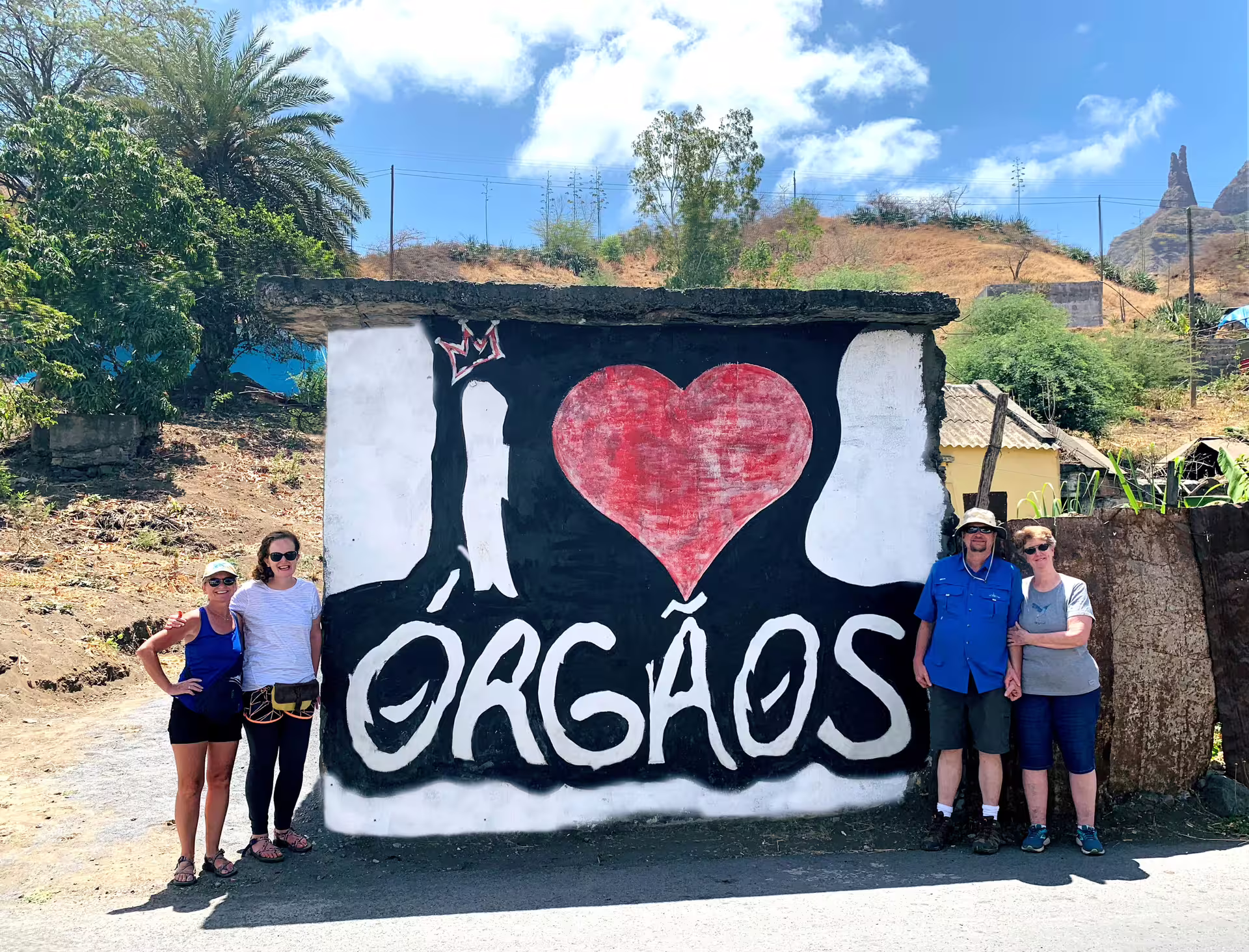 Visitors pose by a vibrant mural saying 'I Love Órgãos,' highlighting cultural exploration on Santiago Island.