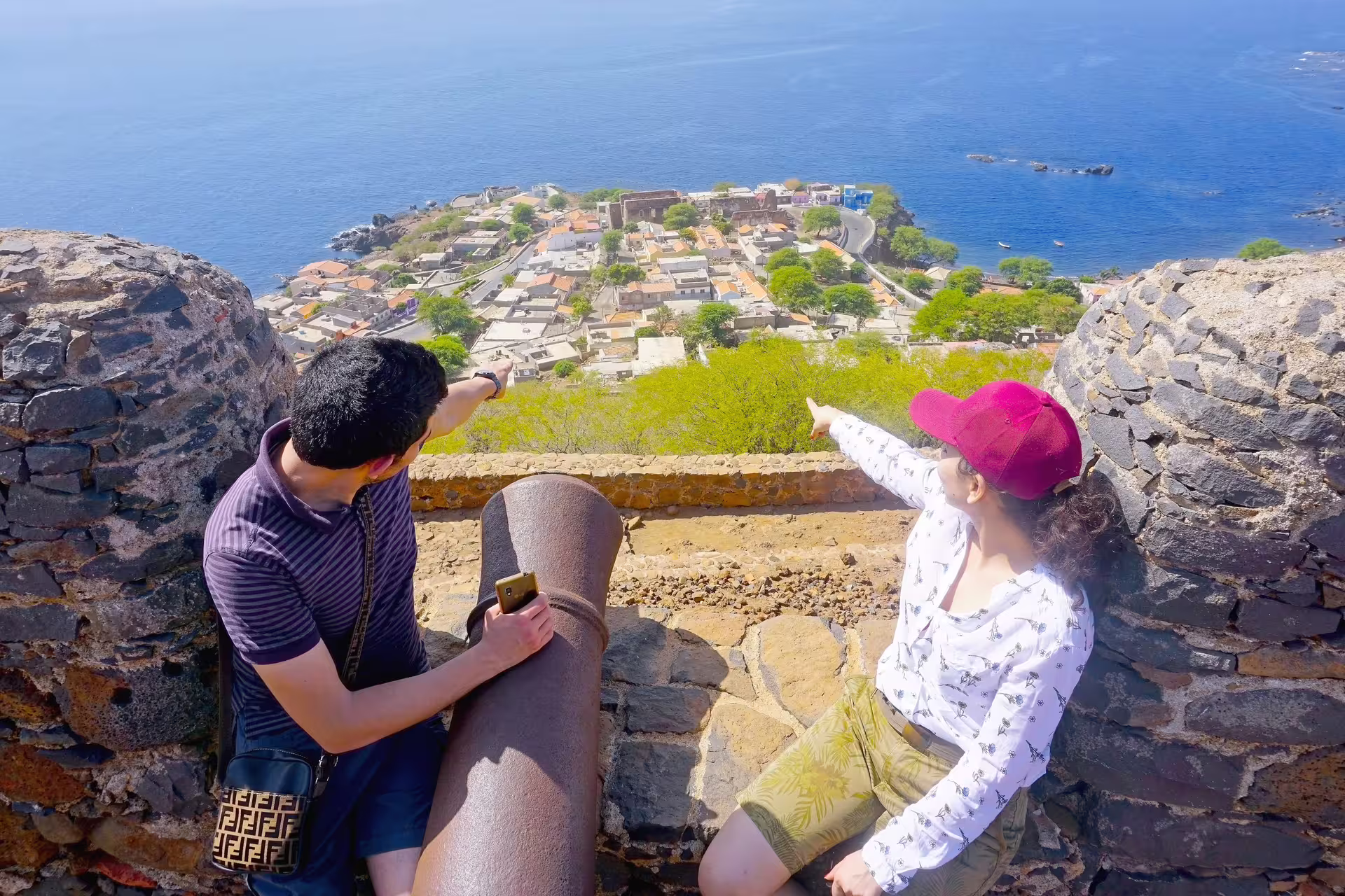Travelers pointing over Cidade Velha coastline from fortress viewpoint, highlight of Santiago Island day tour