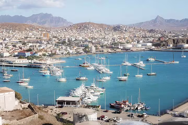 View of Santiago Island's bustling port in Praia with boats anchored against a backdrop of scenic hills and cityscape.