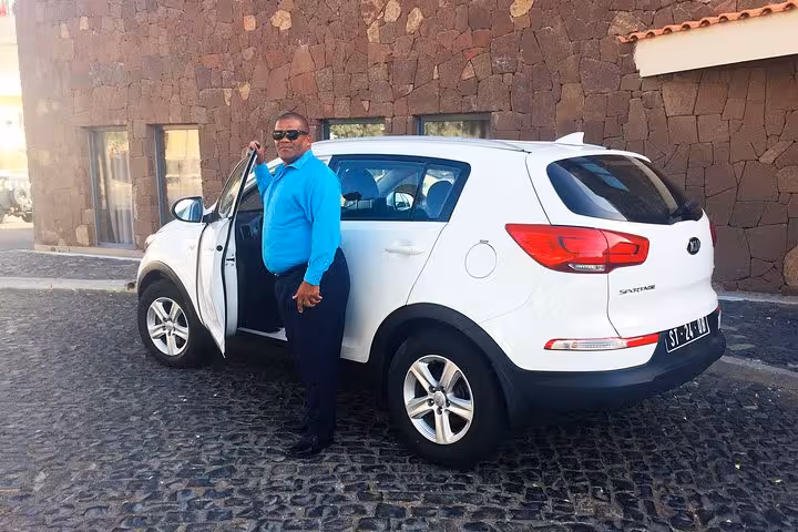 Professional driver in blue shirt standing beside a white Kia Sportage SUV for private transfer in Santiago Island Cape Verde