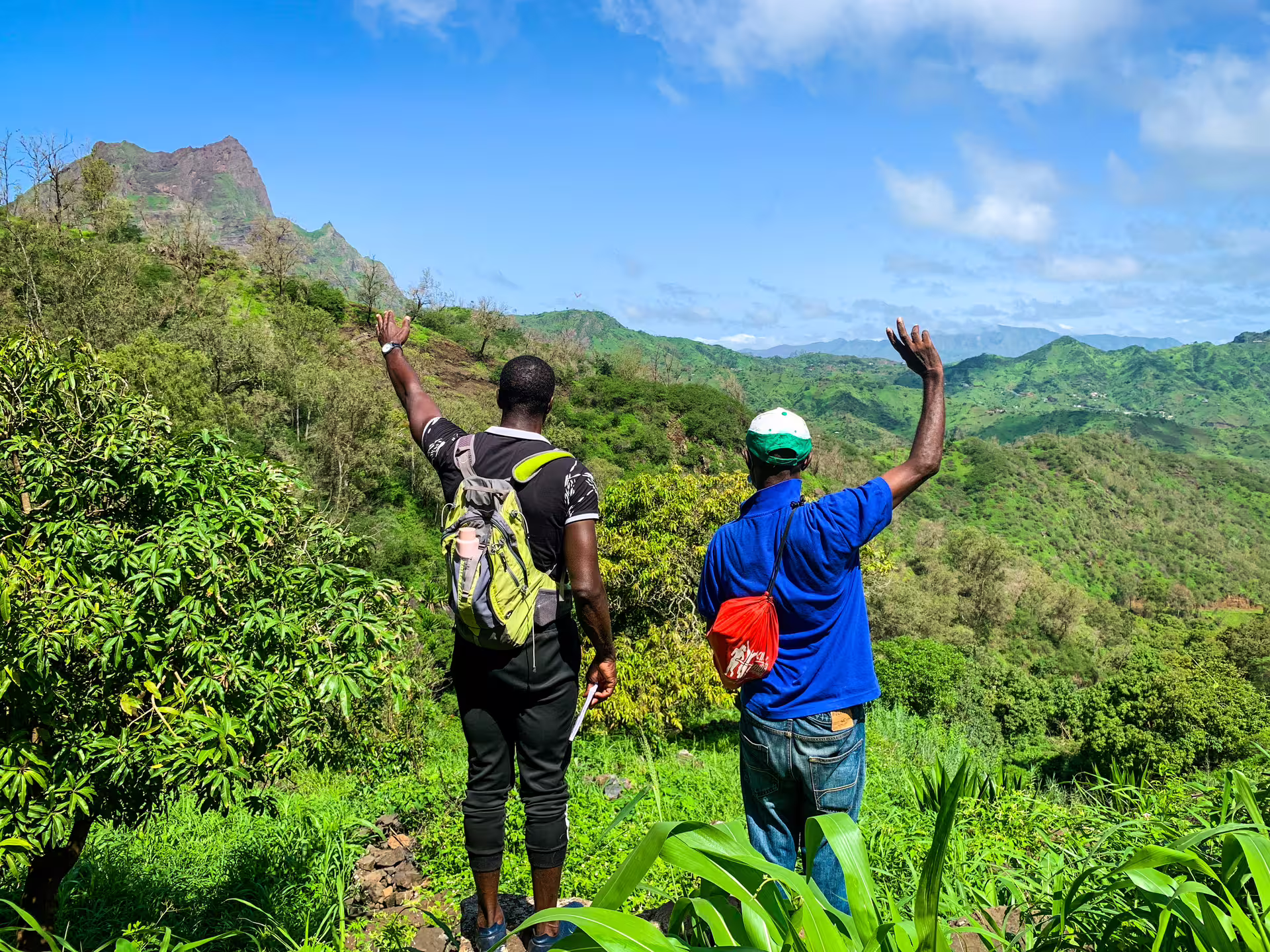 Two hikers waving at the stunning mountainous landscape on Santiago Island's Rui Vaz trail.