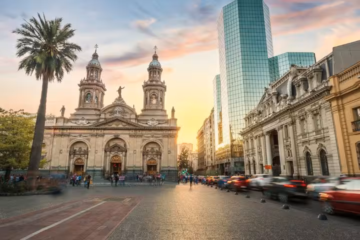 Santiago Cathedral at Plaza de Armas at sunset with busy traffic and modern skyscrapers in background