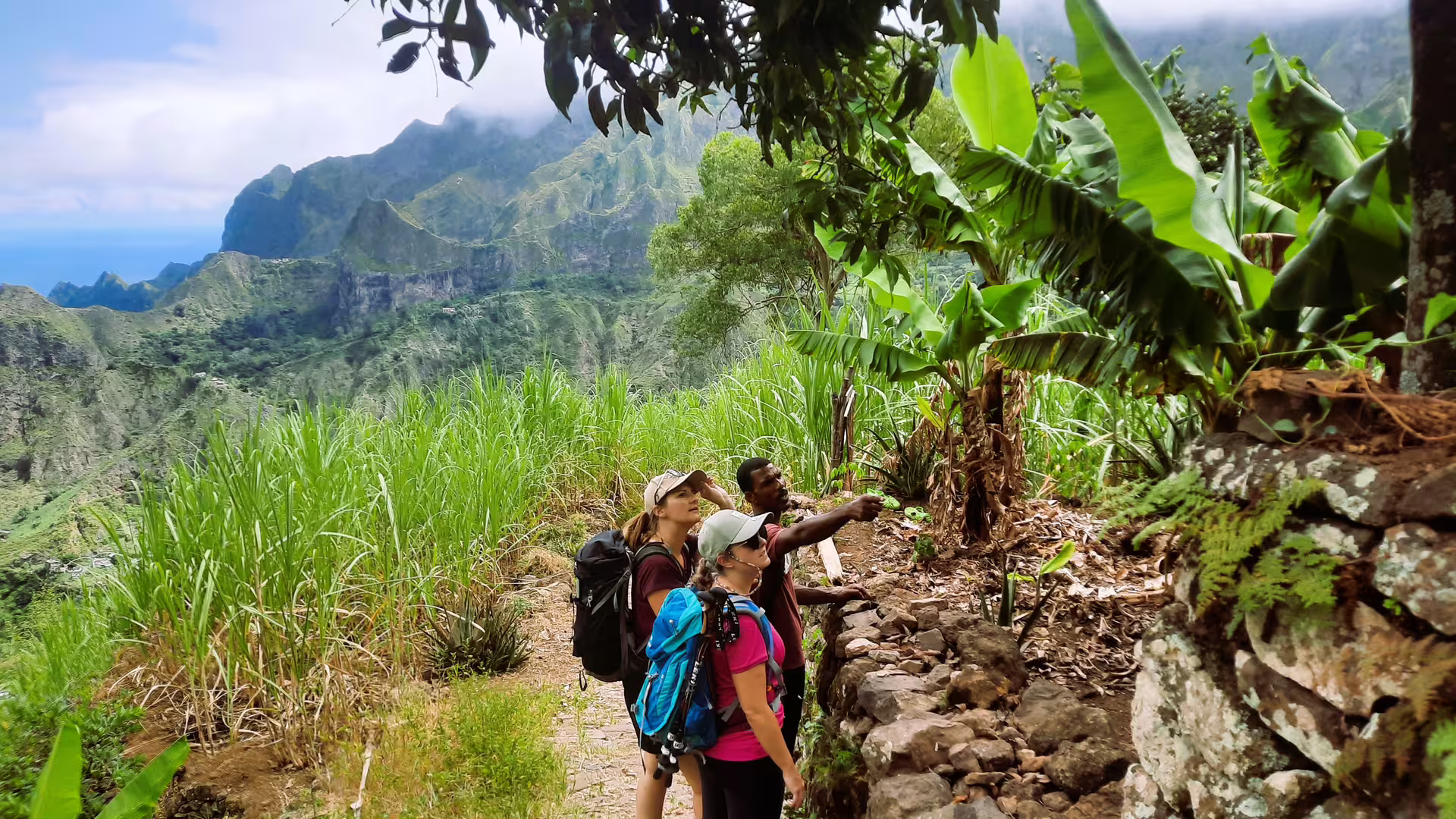 Trekking group exploring lush trails of Cova de Paúl, surrounded by towering mountains and vibrant greenery.