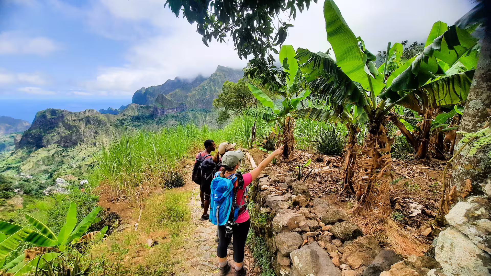 Hikers on a scenic trail in Santo Antão's Cova de Paúl, admiring banana plants and dramatic mountain views.