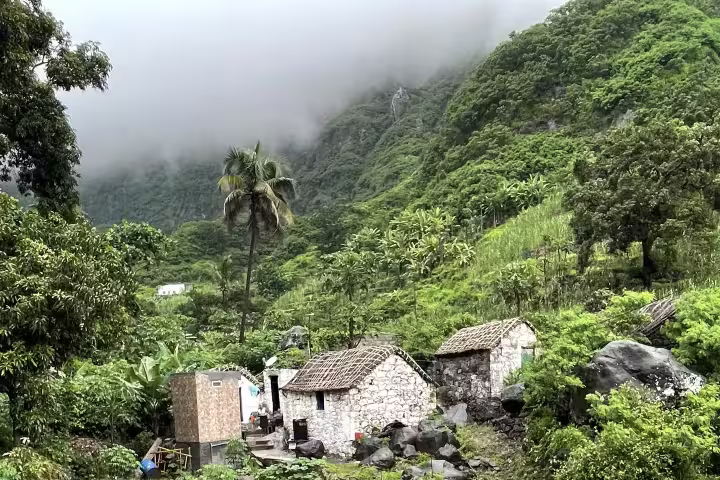 Lush green valley of Santo Antão with traditional stone houses and foggy mountains, perfect for scenic car tours from São Vicente.