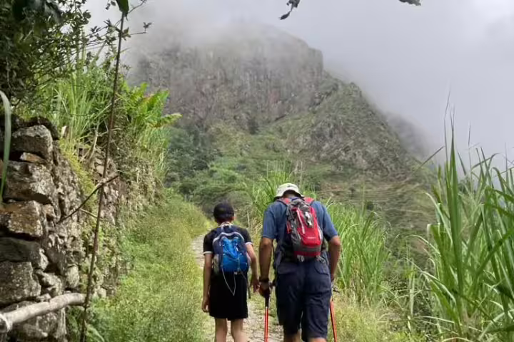 Hikers explore the lush, misty trails of Santo Antão's Valley of Paul, surrounded by verdant mountains and rugged terrain.