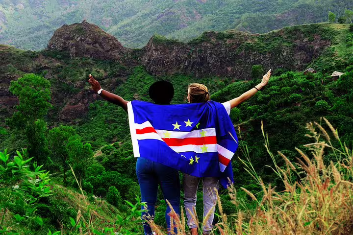 Two people with a Cape Verde flag enjoy panoramic views of Santo Antão's lush volcanic landscape.