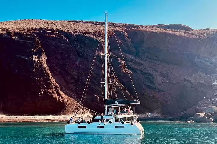 Catamaran sailing near Santorini's rugged coastline on a premium half-day cruise with views of iconic cliffs.