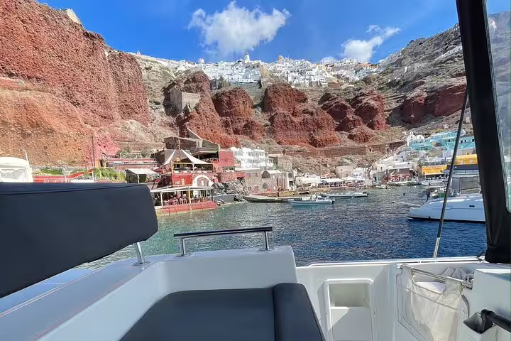 View from a catamaran of Santorini's colorful cliffs and charming architecture under a bright blue sky.