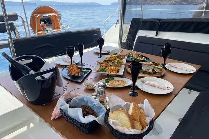 Exquisite lunch spread on a catamaran deck, featuring seafood and wine, during a Santorini private cruise.