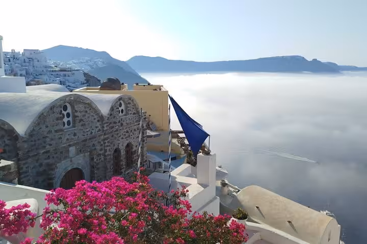 Santorini cave church and bougainvillea overlooking the misty caldera, iconic stop on a one-day Santorini tour