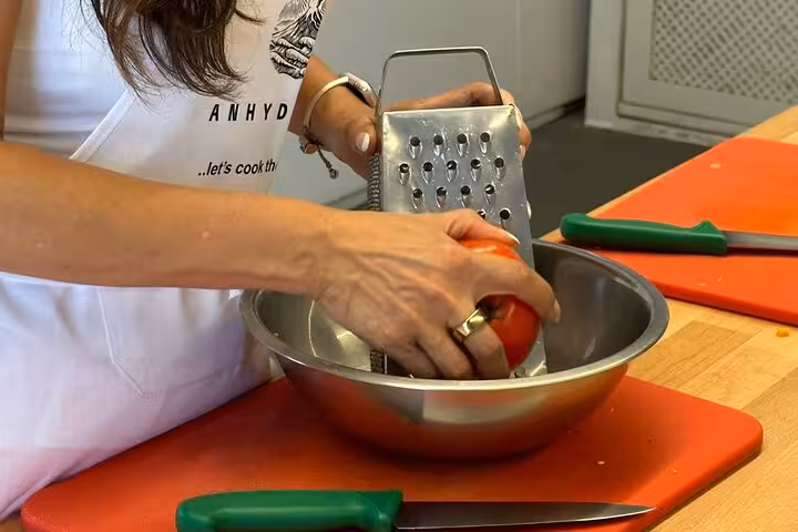 Hands grating fresh tomato for Santorini cooking class, preparing Greek salad and meze during private island tour
