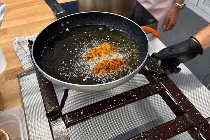 Greek fritters frying in pan during Santorini cooking class, part of honeymoon tour with 2 winery visits