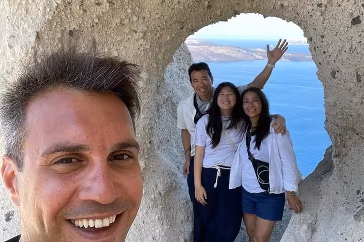 Family photo in volcanic rock arch overlooking Santorini caldera, perfect stop on cruise ship day tour
