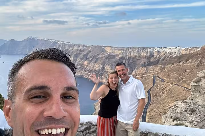 Couple with local guide at Santorini caldera overlook, scenic cliffside views on one-day cruise ship tour