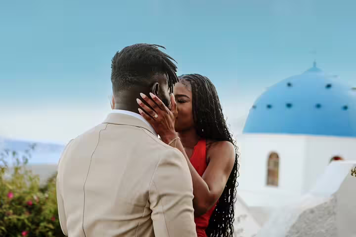 Romantic Santorini engagement photoshoot with personal proposal photographer, couple kissing by blue dome church