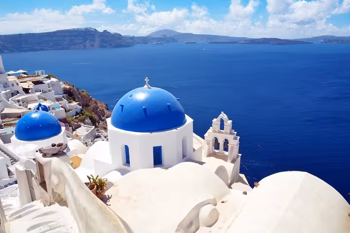 Blue-domed churches of Santorini with white-washed buildings overlooking the deep blue Aegean Sea in Fira