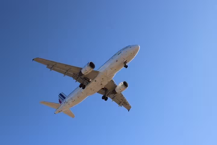 Airplane flying overhead against blue sky, ideal for One Day Escape to Enchanting Santorini flight tour