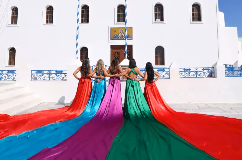 Friends in colorful flying dresses at a white Santorini church, private tour photoshoot in Greece