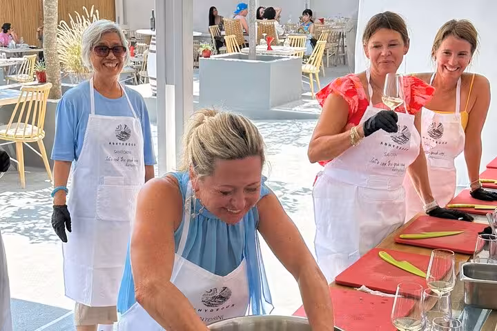 Guests in aprons enjoy Santorini honeymoon cooking class, smiling with wine before 2 winery tastings