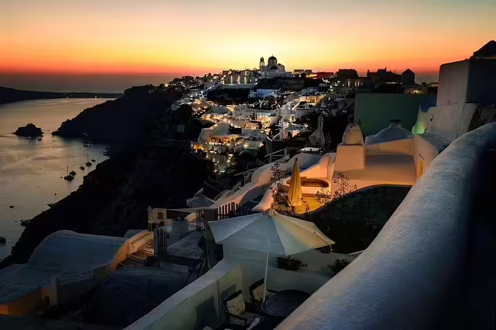 Sunset view of illuminated Santorini village at night, featuring iconic white architecture overlooking the Aegean Sea.
