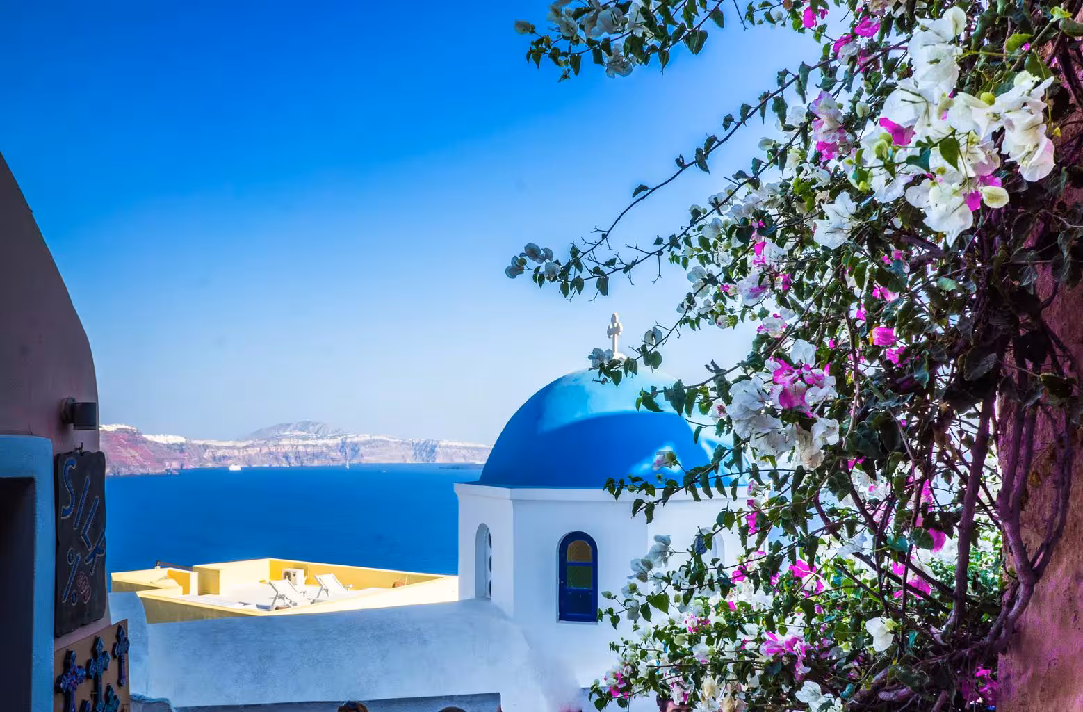 Blue-domed church in Oia with bougainvillea and caldera sea views on a Santorini highlights private tour