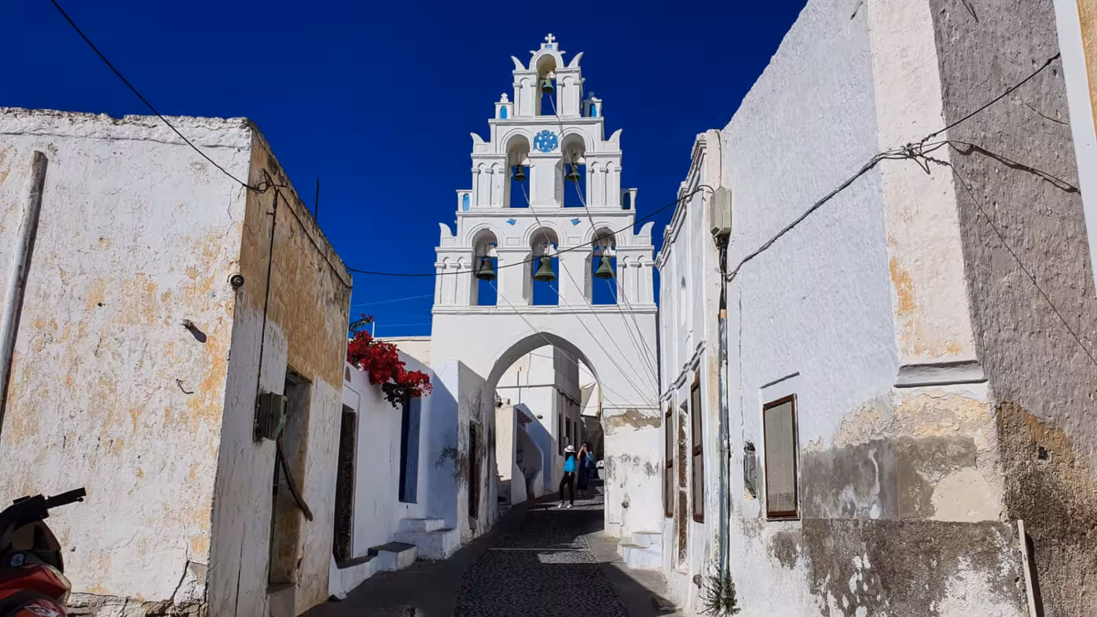 Semi-private Santorini panoramic tour stop at Pyrgos village, white bell tower arch and cobblestone lane