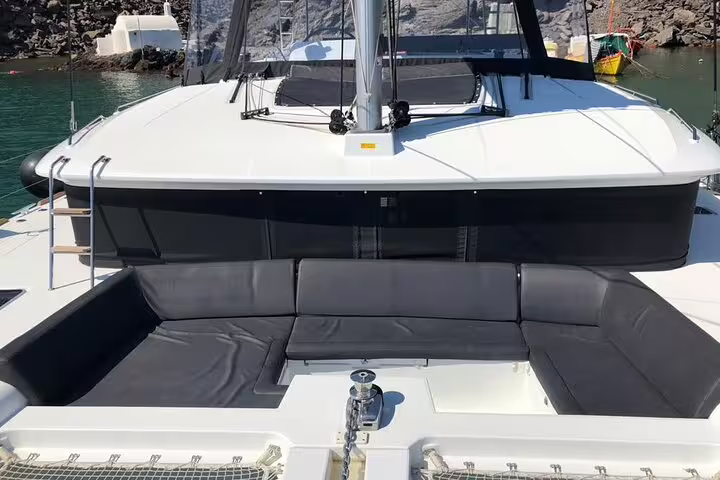 Luxurious catamaran deck with comfortable seating overlooking the serene waters of Santorini on a private cruise.