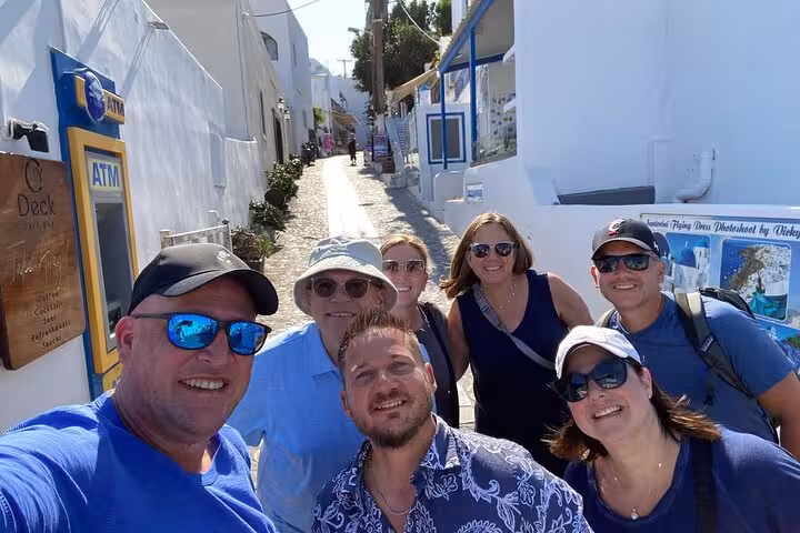 Small group on a Santorini private tour walking a sunlit Cycladic alley in Oia with blue-and-white buildings