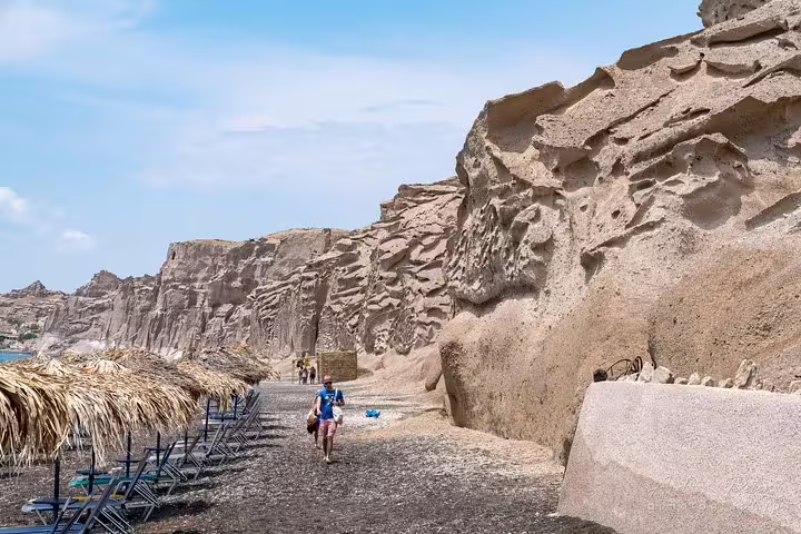 Tourists explore the unique volcanic rock formations and tranquil beach on a private full-day sightseeing tour in Santorini.