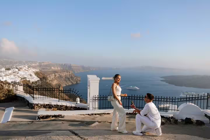 Santorini caldera proposal captured by personal photographer, groom kneels with ring at cliffside viewpoint