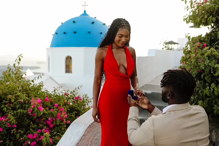Santorini proposal photographer captures man kneeling with ring by blue dome church in Oia at sunset