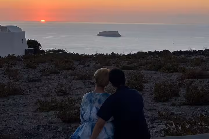 Couple watching Santorini caldera sunset on a private honeymoon wine tour with romantic Aegean sea views